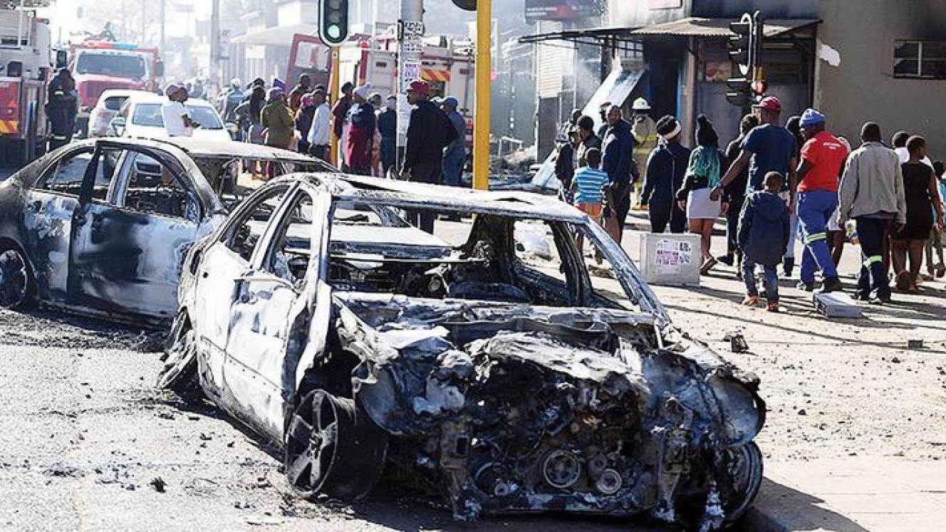 Pedestrians pass the burnt wreckages of cars destroyed in the spate of xenophobic violence.
