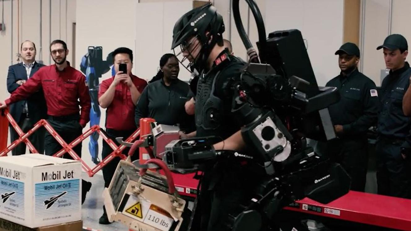 A Delta Airlines employee tests an exoskeletal robotic strength augment system while colleagues look on.