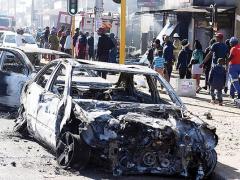 Pedestrians pass the burnt wreckages of cars destroyed in the spate of xenophobic violence.
