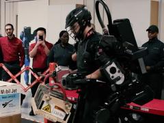 A Delta Airlines employee tests an exoskeletal robotic strength augment system while colleagues look on.