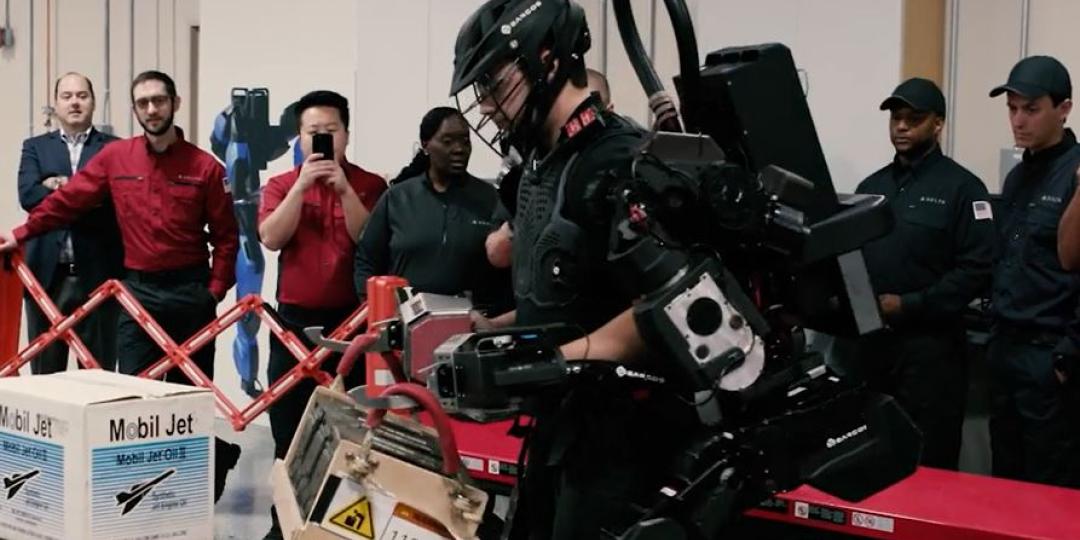 A Delta Airlines employee tests an exoskeletal robotic strength augment system while colleagues look on.