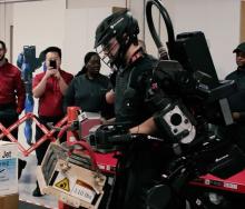 A Delta Airlines employee tests an exoskeletal robotic strength augment system while colleagues look on.